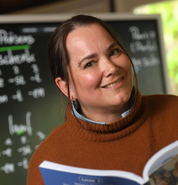 Irene Tagmi im Portrait mit einem Buch in den Händen und der Tafel im Hintergrund