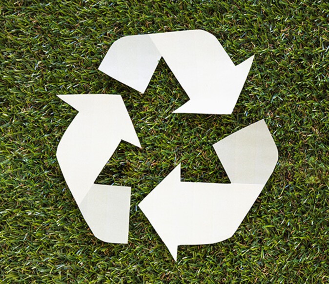 Ein weißes Recycling-Logo liegt auf kurzem Gras
